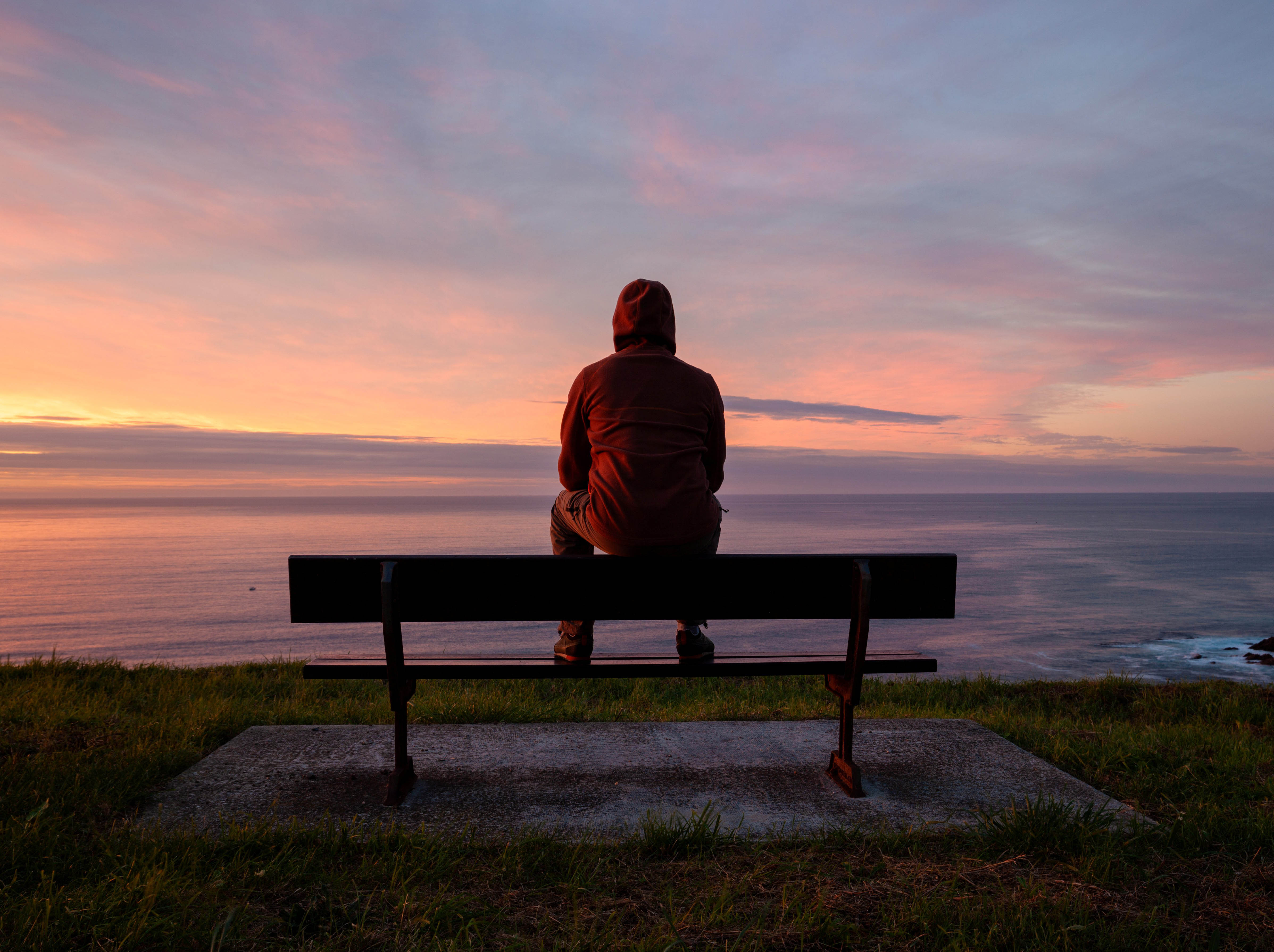 person sitting on bench alone overlooking sunset ocean view