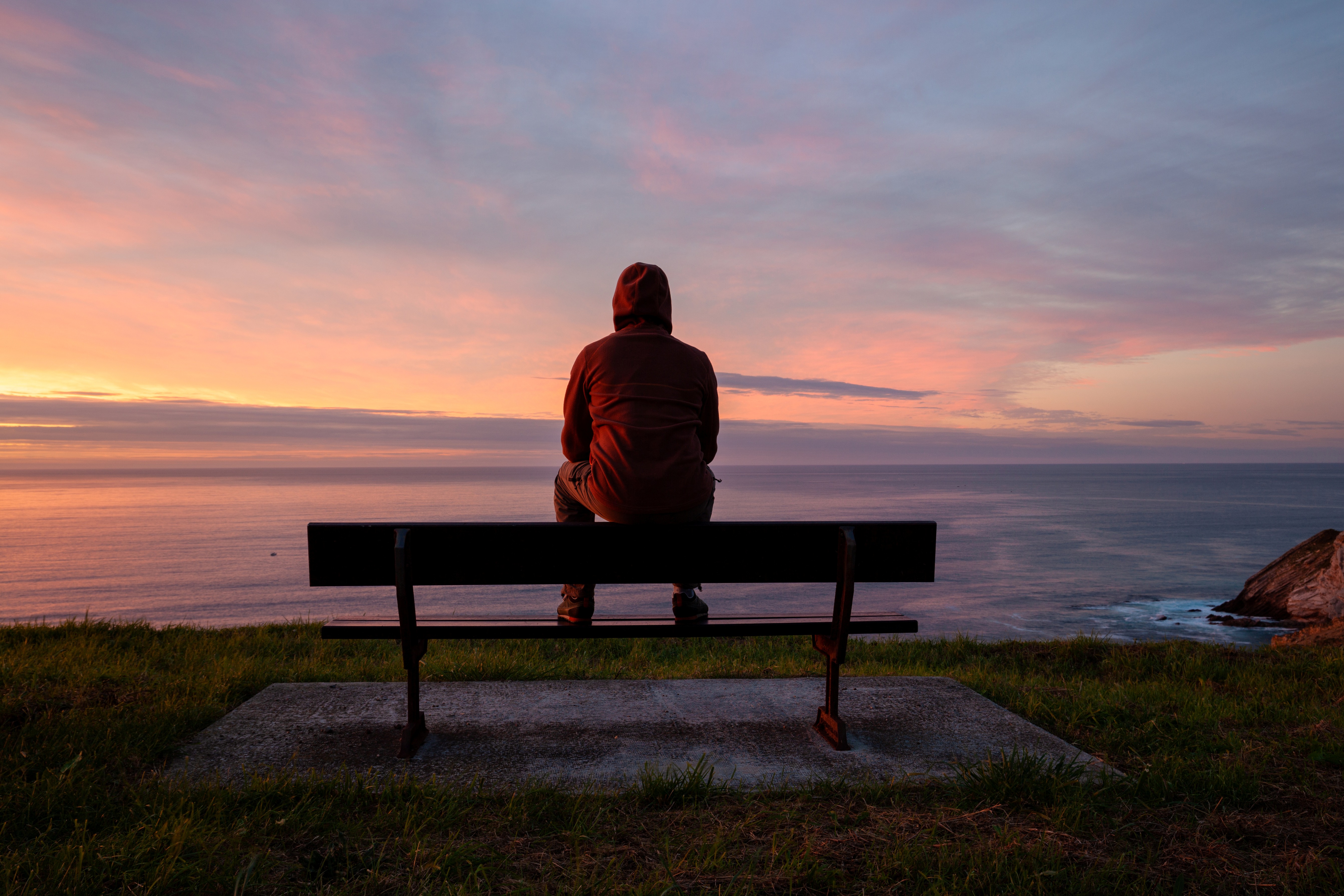 person sitting on bench alone overlooking seascape with sunset