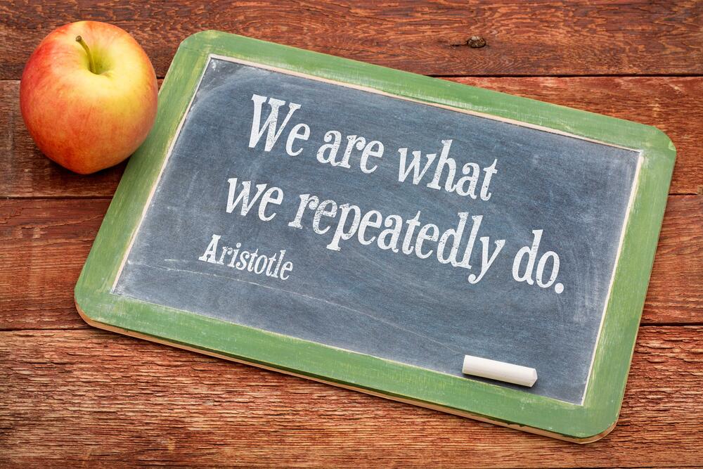 Apple with a chalkboard next to them that says "We are what we repeatedly do." 