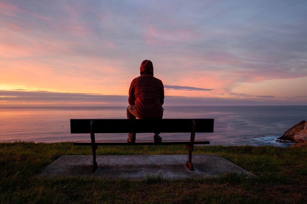 person sitting on bench alone overlooking seascape with sunset