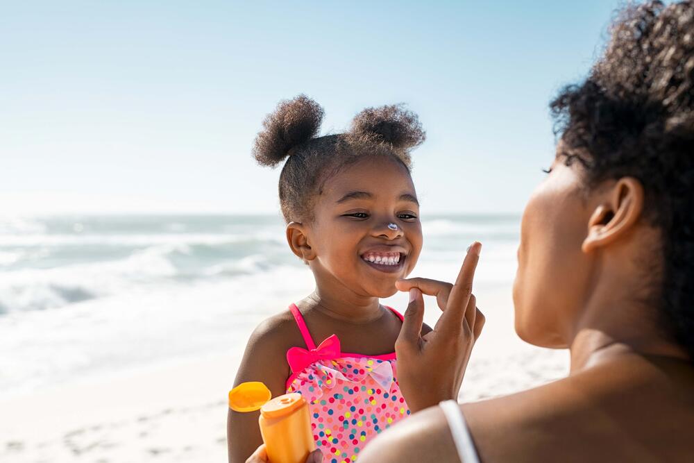 mother applying sunscreen to young daughter at the beach