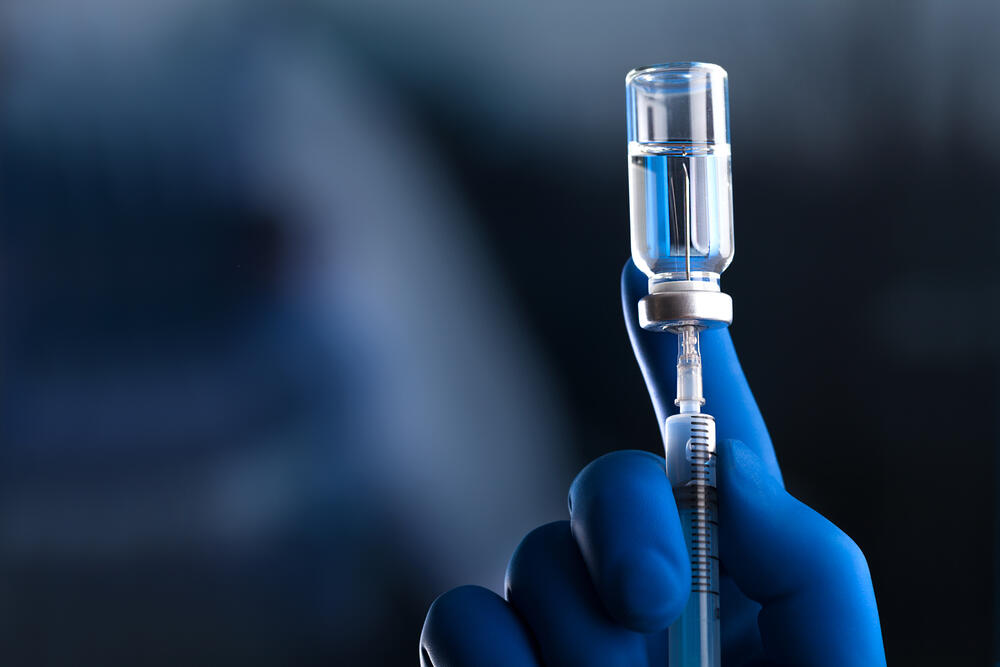gloved hand drawing vaccine out of vial using a needle