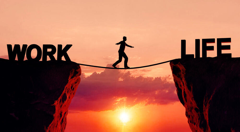 Silhouette of person walking a tightrope on a cliff with the "work" on one side of the chasm and "life" on the other side