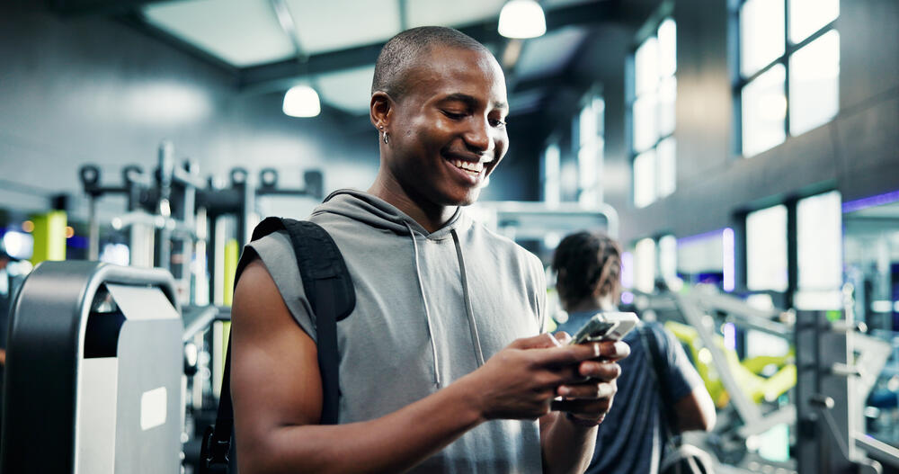 Man smiling in gym using smartphone